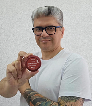 Foto mostra Mago dos cabelos, que sorri e mostra pote vermelho de Dose Fortalecedora Force System Aneethun 25g.