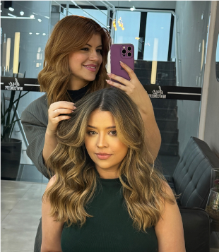 Foto mostra Hairstylist Vih Lopes manejando cabelo de modelo em seu salão. A modelo tem cabelos em tom de caramelo, de lisos para ondulados.