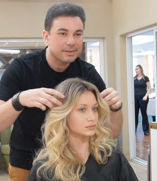 Foto mostra Hairstylist Robson Jassa manejando cabelo de modelo em seu salão. A modelo é loira e tem cabelos lisos para ondulados.