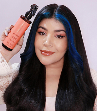 Foto mostra Influencer Carol Kyoko, com cabelos longos e pretos, com mecha azul na franja, segurando Spray Acidificante Antidanos Restore System Aneethun 210mL